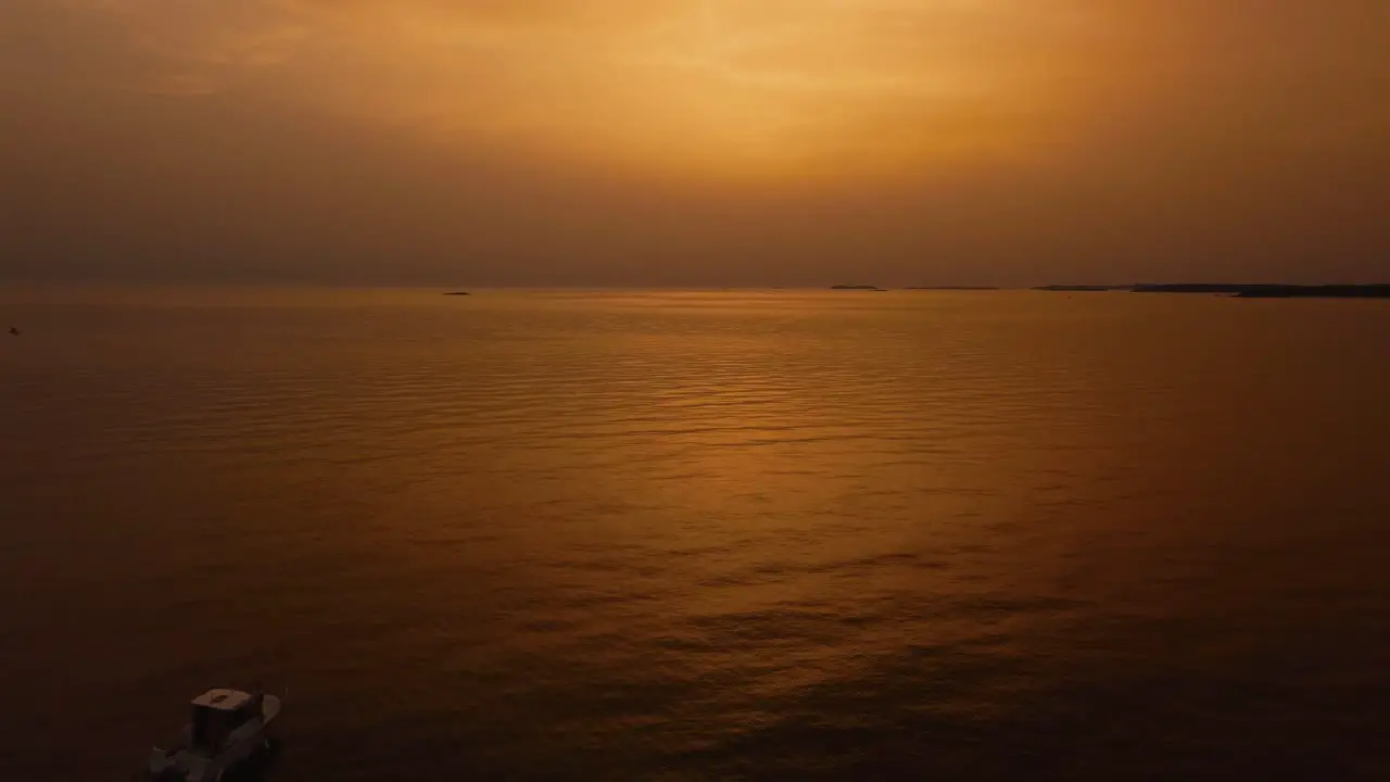 Flying backwards above a vacation yacht ship fishing boat by beautiful orange and red sunset seaside bay in the idyllic Adriatic mediterranean sea ocean by the Croatian coast