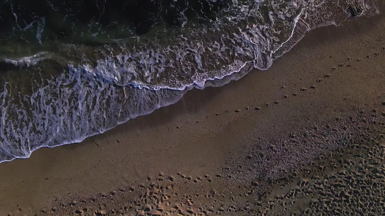 Aerial view of waves at the beach moving closer to the ground and tilting up into the horizon