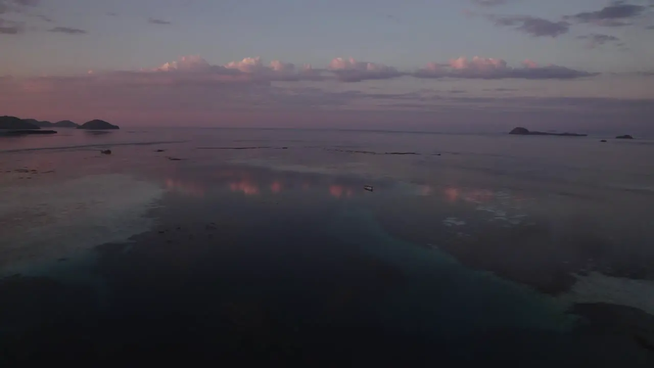 Pink Purple Sunset Over the Sea Near Komodo Island with Colorful Clouds Reflecting in Shallow Calm Water Aerial Side Dolly