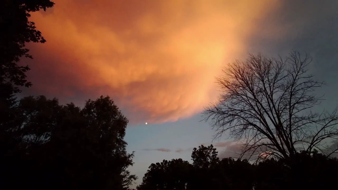 Pan across evening sky with moon and dramatic storm clouds at sunset