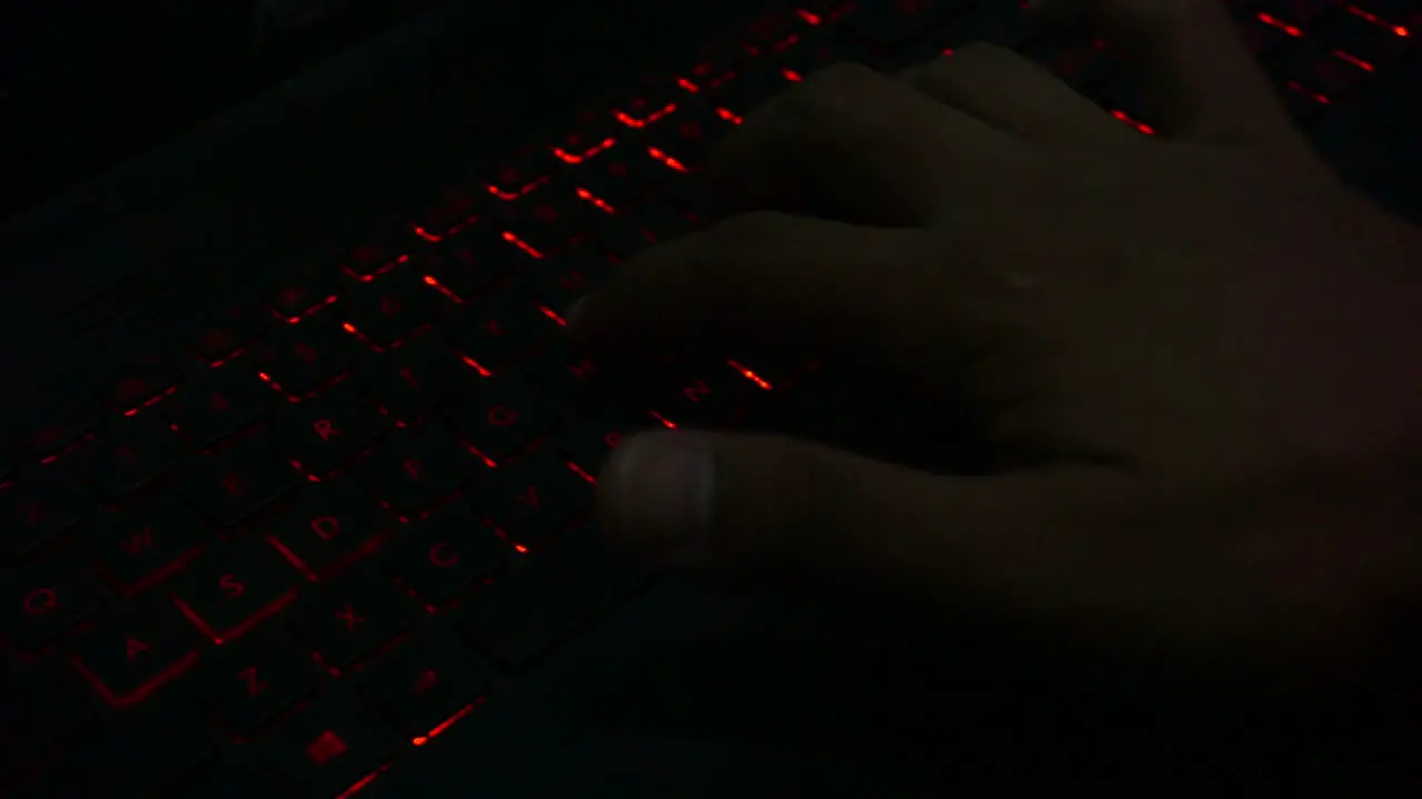 Top view of hand typing on red lighting keyboard of laptop in dark room close up shot-1