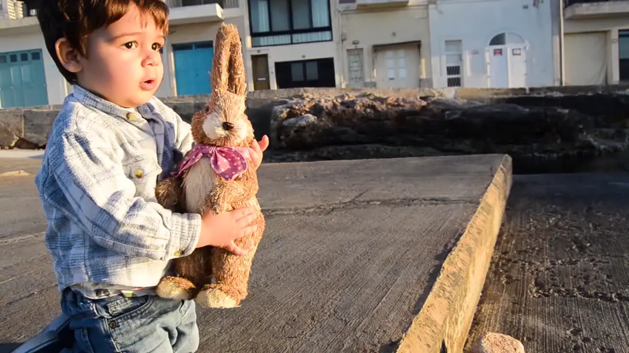 Cute little boy in jeans playing with his brown bunny rabbit with light from sunset