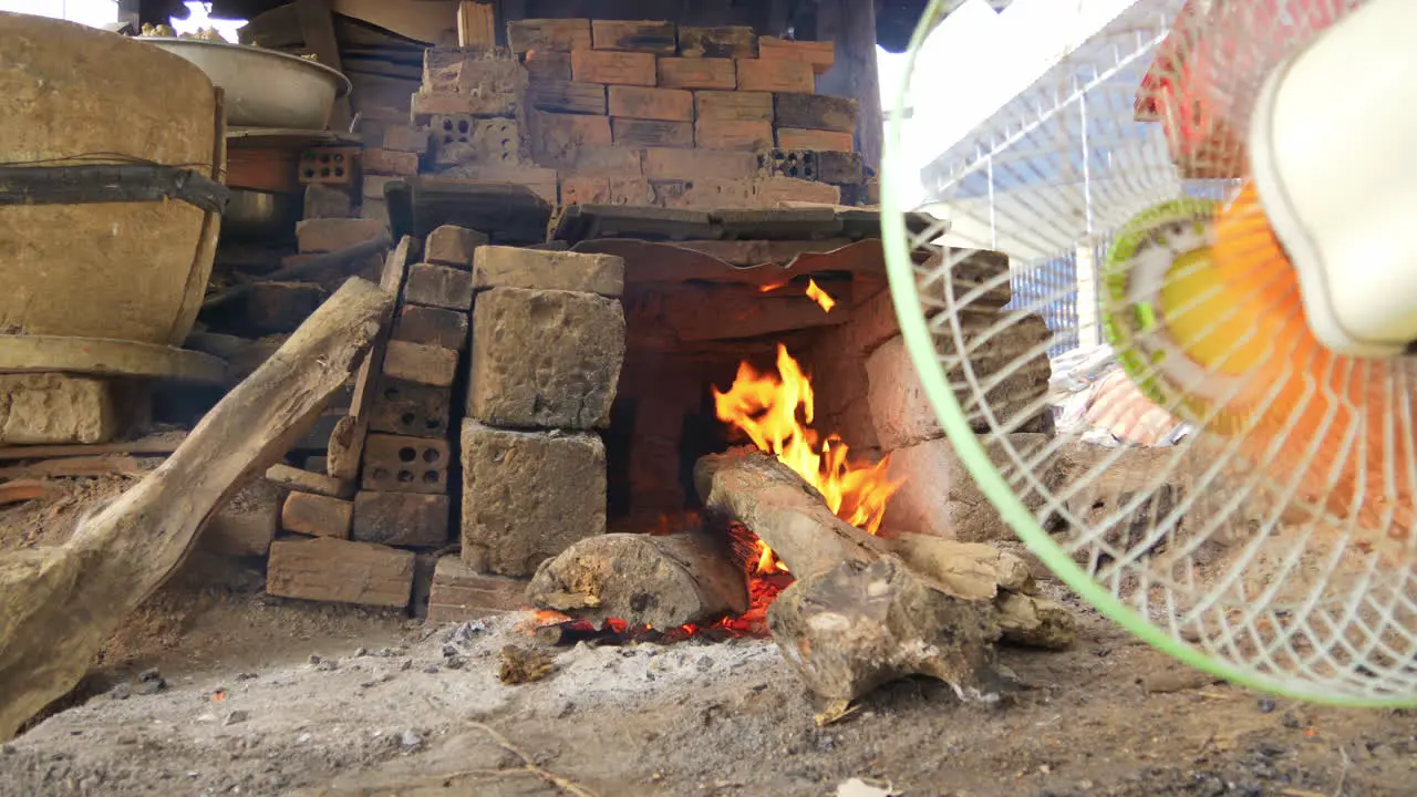 Low wide view of raging wood fire in pottery kiln fan blows fire Than Ha Hoi An Vietnam