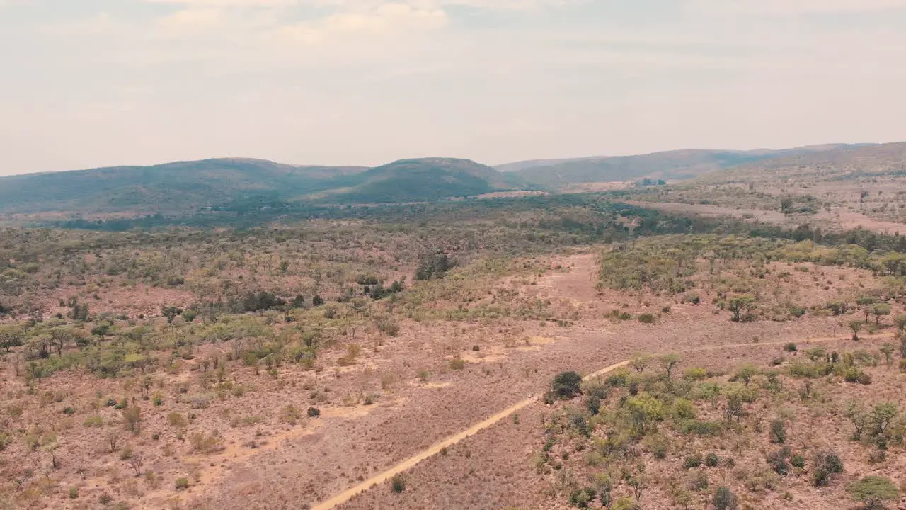 Dirt road in african savannah bush with trees and hills drone shot