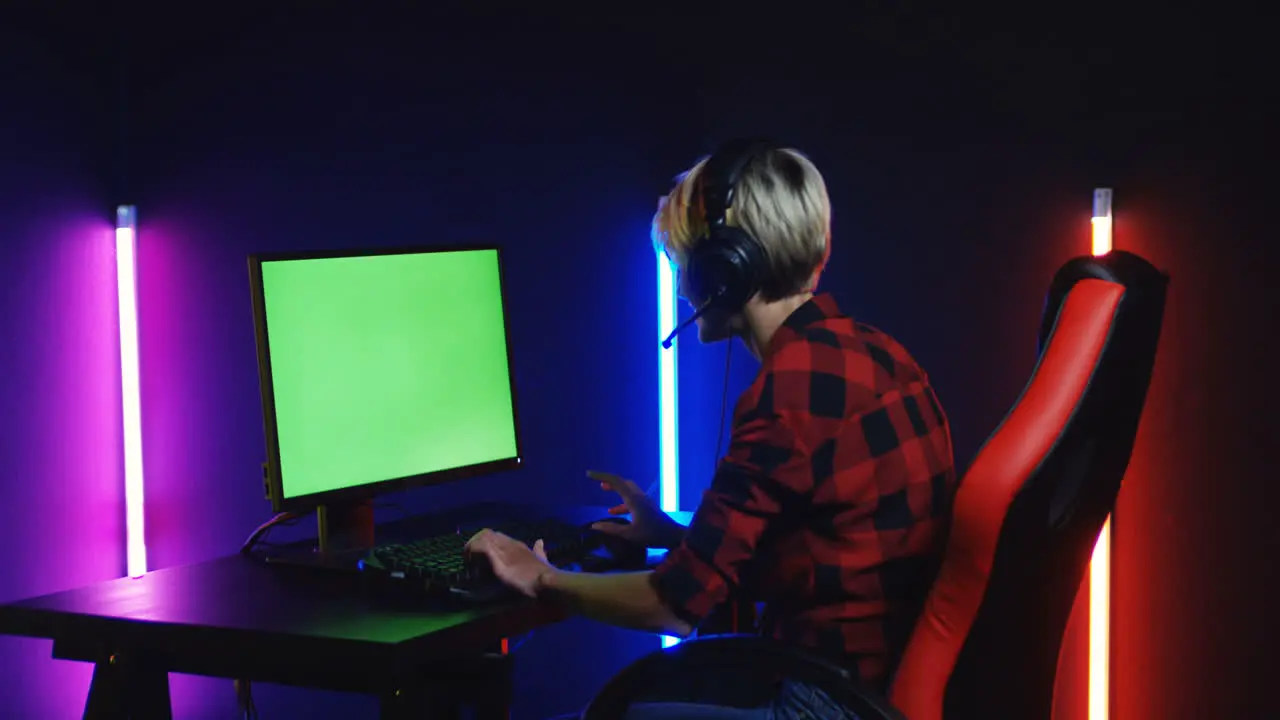 Young Woman Playing On The Computer With Chroma Key Screen And Celebrating A Victory In A Room With Colorful Neon Lamps On The Wall