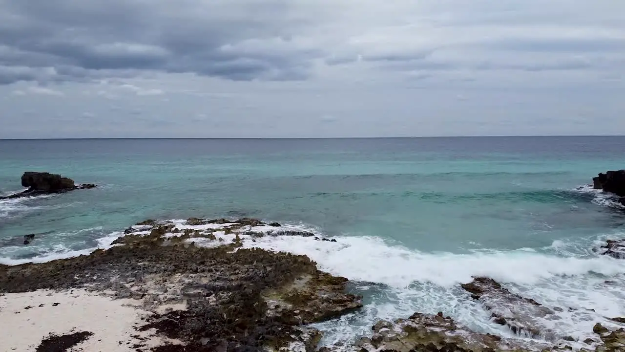 Aerial drone flying from a rocky and white sand beach towards a rough but clear Caribbean Sea in Cozumel Mexico