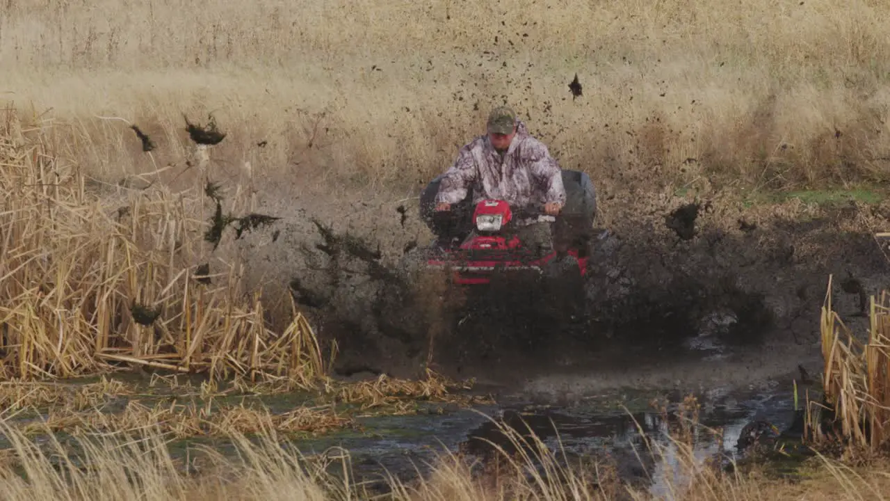 Man riding quad ATV into mud swamp had on with mud flying everywhere