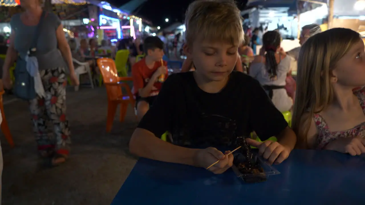 Boy eating a scorpion accompanied by family at a local market in Khao Lak Thailand