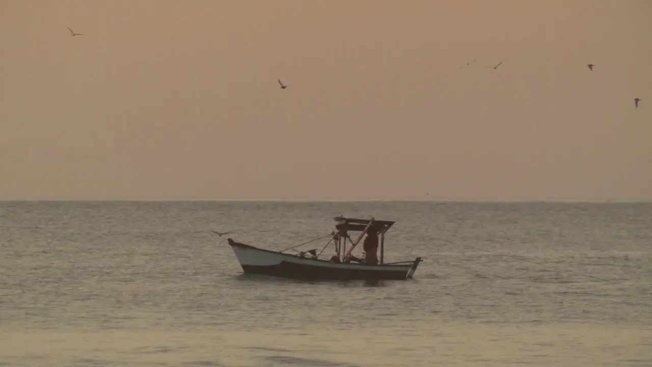 Fisherman Fishing in Small Boat on Sea Golden Sky Background Dusk