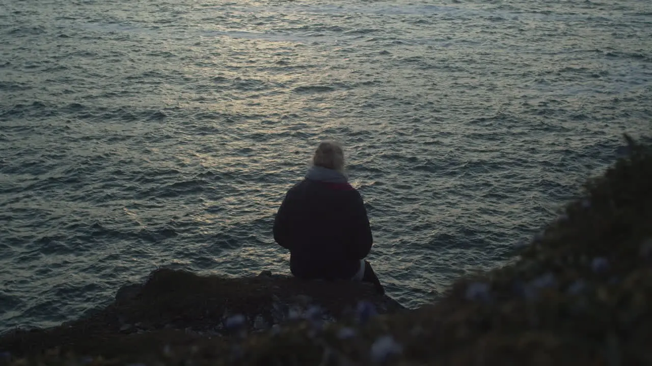 Woman Sitting At The Edge Of A Hill Overlooking The Sea In Sunset medium shot