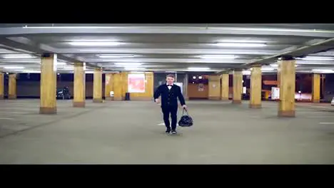 Young blonde businessman in a black suit with bow-tie walking on the parking with big leather bag Slow Motion