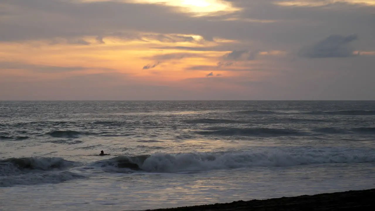 Man paddling out at sunset to surf with woman running by on beach