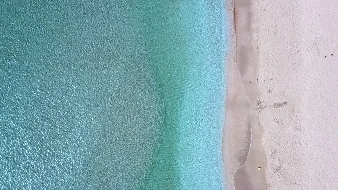 Top-down aerial view of an empty tropical white sands beach and water as it ripples gently in the sun