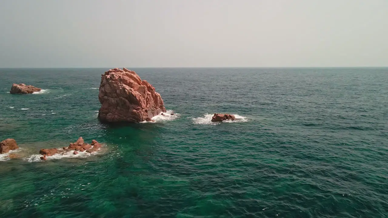 Big Red Rocks With White Waves Crashing In The Ocean Of Sardinia Italy At Daytime aerial drone shot