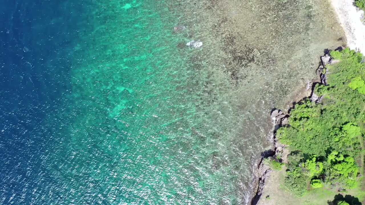 Aerial bird's eye view above turquoise tropical water with barrier reef near a coastline with green trees around travel concept