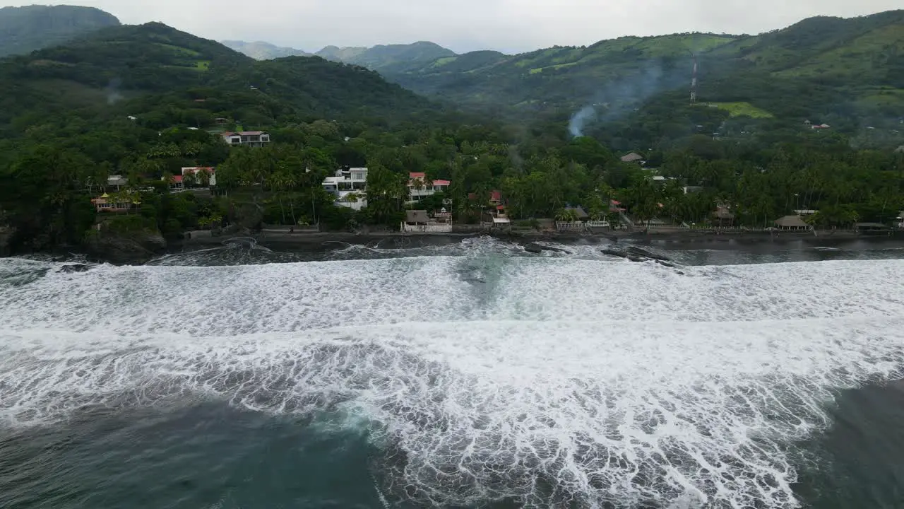 Aerial view moving left shot scenic view of houses on the shoreline of the bitcoin beach in El Salvador Mexico mountain ranges in the background