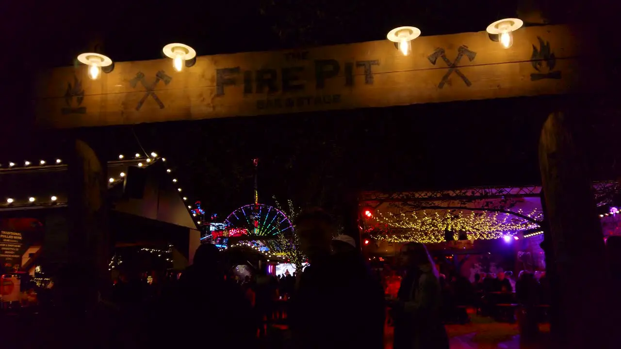 Shot of crowd walking into the entrance of an amusement park in London UK at night time with rides