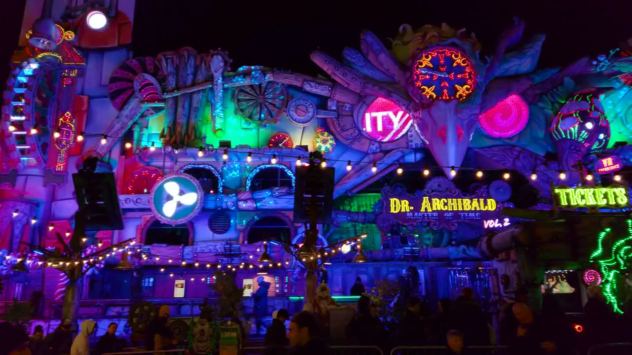 Pan shot of colorful amusement park ride inside amusement park at night time in London UK with locals walking around