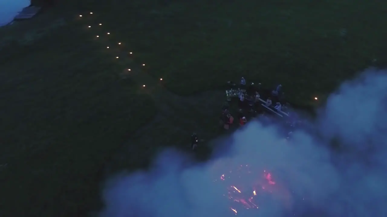 People Enjoy Massive Bonfire At Night in a meadow field Aerial Fly Away View