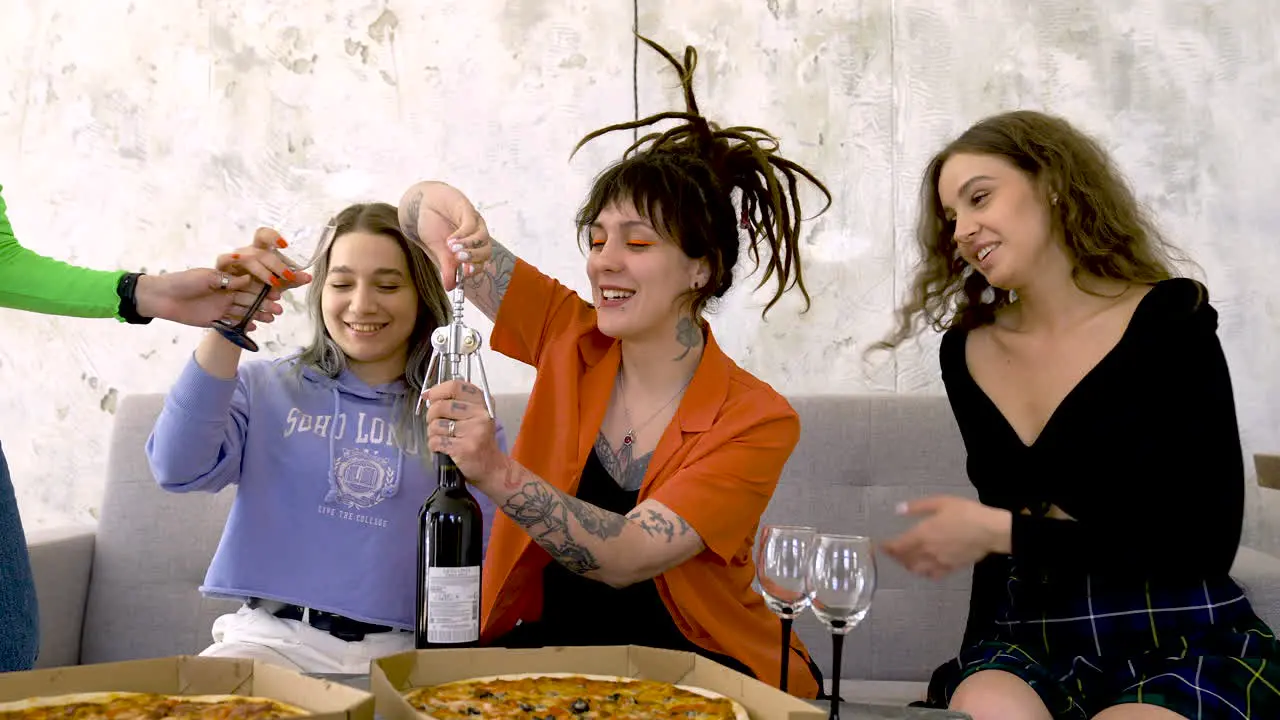 Chica Alegre Con Tatuajes Y Rastas Abriendo Una Botella De Vino Mientras Se Divierte En Una Fiesta Con Amigos Y Comparte Pizza En Casa