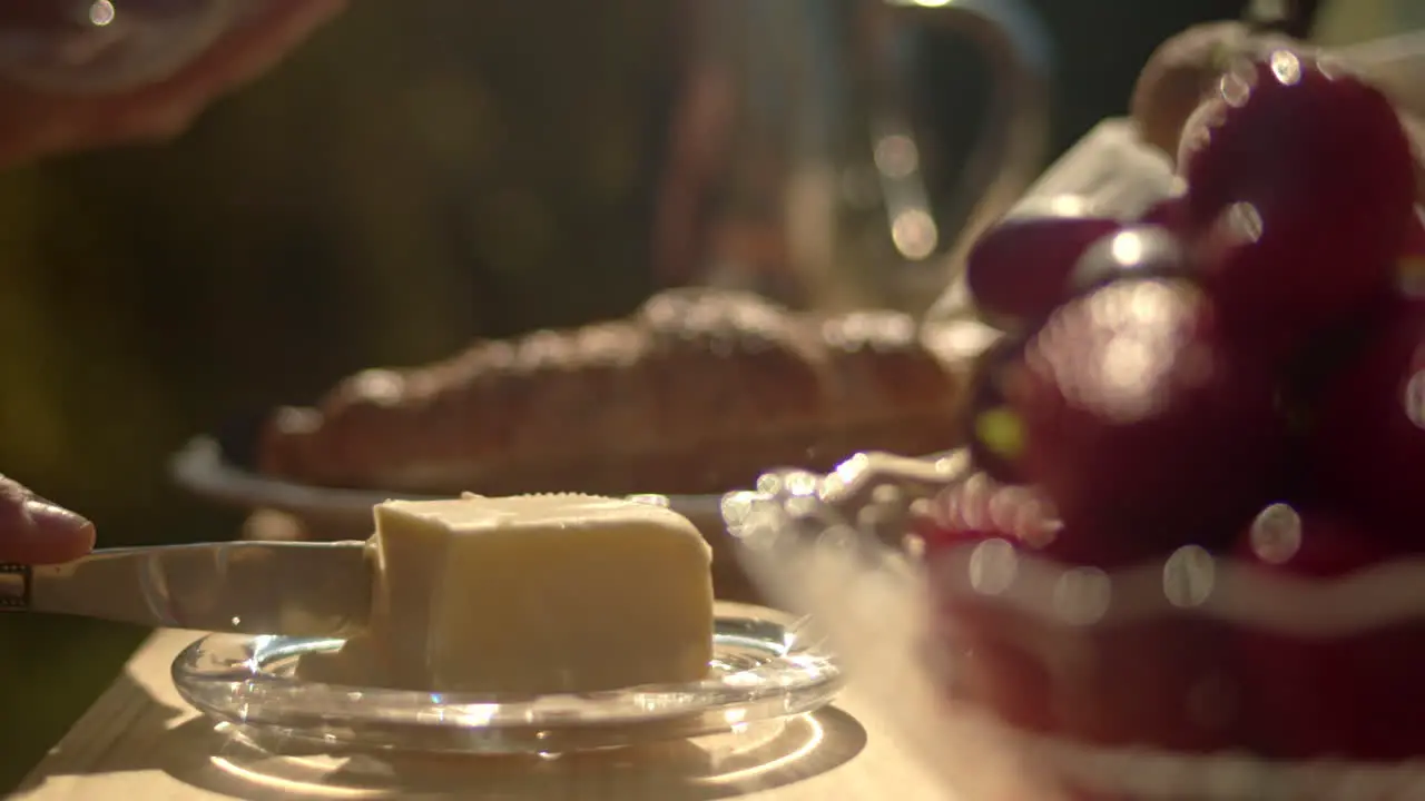 Lifting butter dish on outdoor table to slice and spread on toast in background