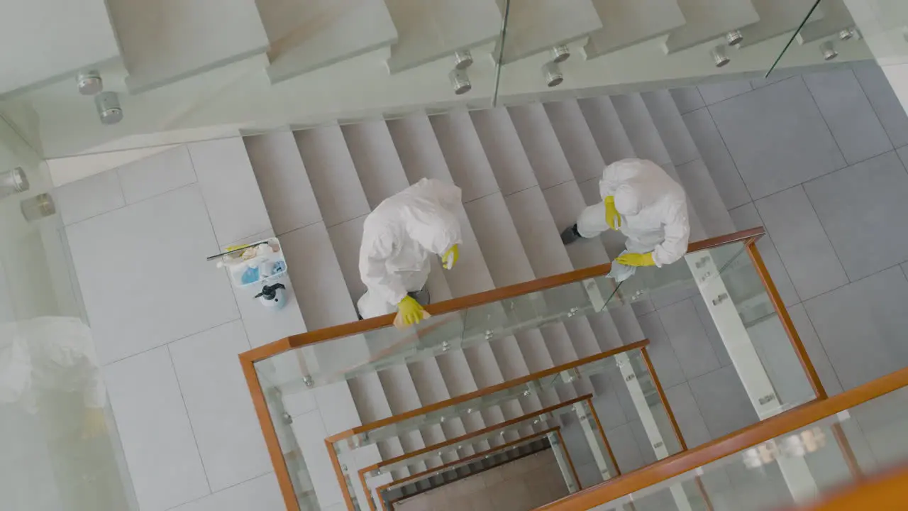 Vista Superior De Dos Hombres De Limpieza Que Usan Equipo De Protección Personal Limpiando Barandillas De Escaleras Dentro De Un Edificio De Oficinas