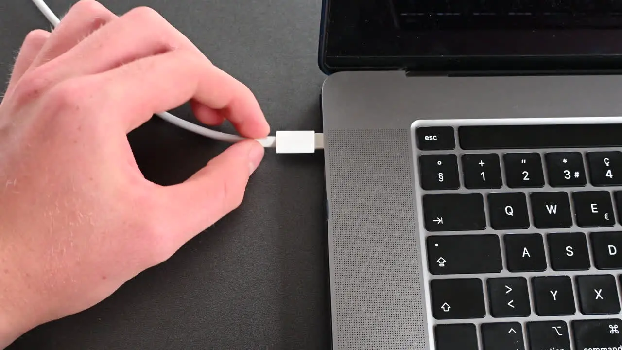 A laptop user plugs in a cable to charge his computer's battery