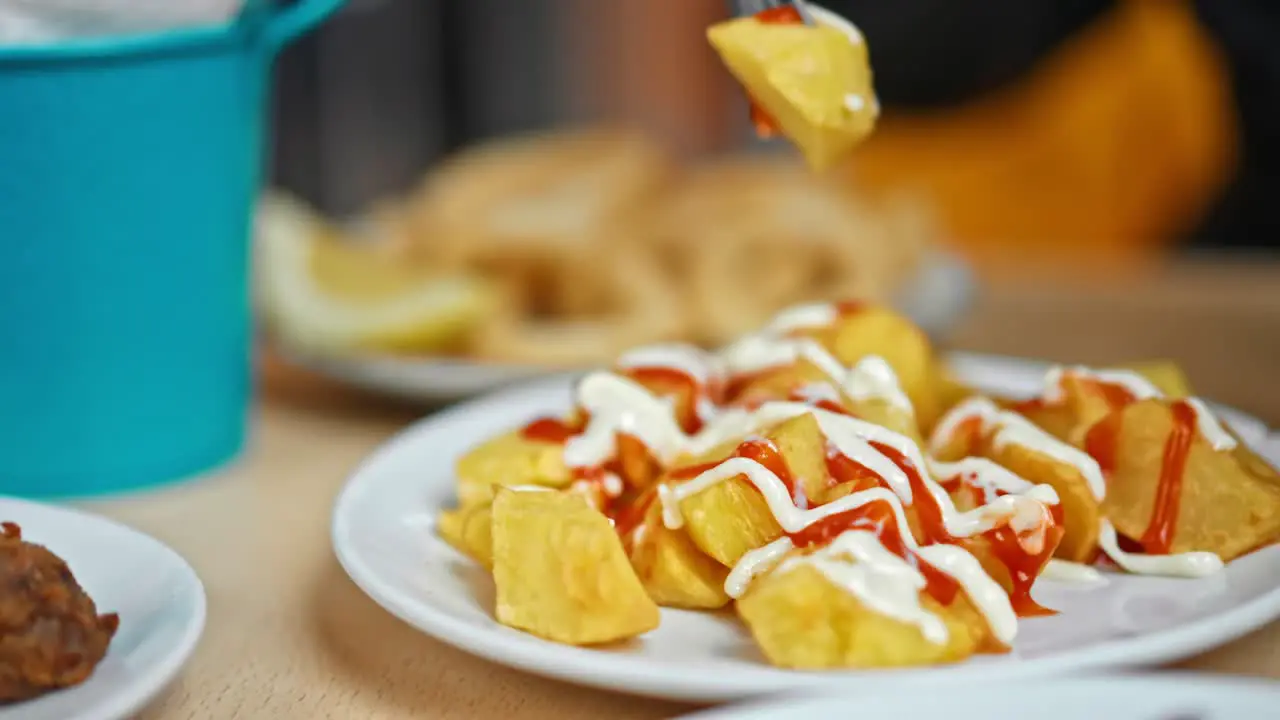 Close up on typical Spanish dish "Patatas Bravas" fork rise a roasted potatoes with ketchup and mayonnaise on it