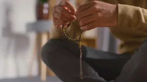 Close Up Of Muslim Man Praying Holding Prayer Beads Sitting On Floor At Home