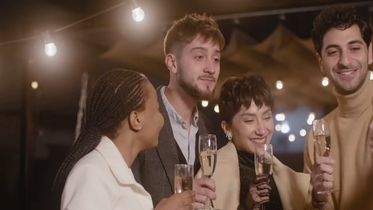 Portrait Of Group Of Four Happy Multiethnic Friends Holding Champagne Glasses And Taking A Selfie Video At New Year's Eve Party