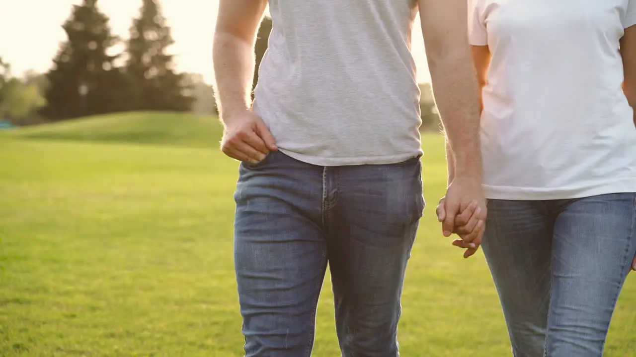 Close Up Of An Unrecognizable Couple Holding Hands And Walking Together Towards Camera On Meadow In The Park