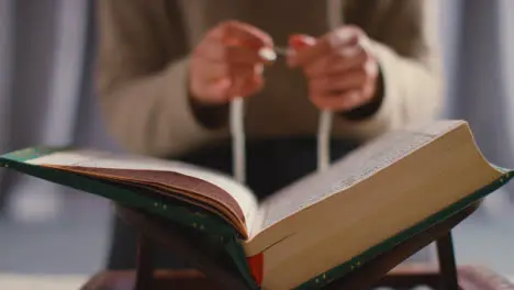 Close Up Of Muslim Woman Praying With Prayer Beads Over Open Copy Of The Quran At Home 1