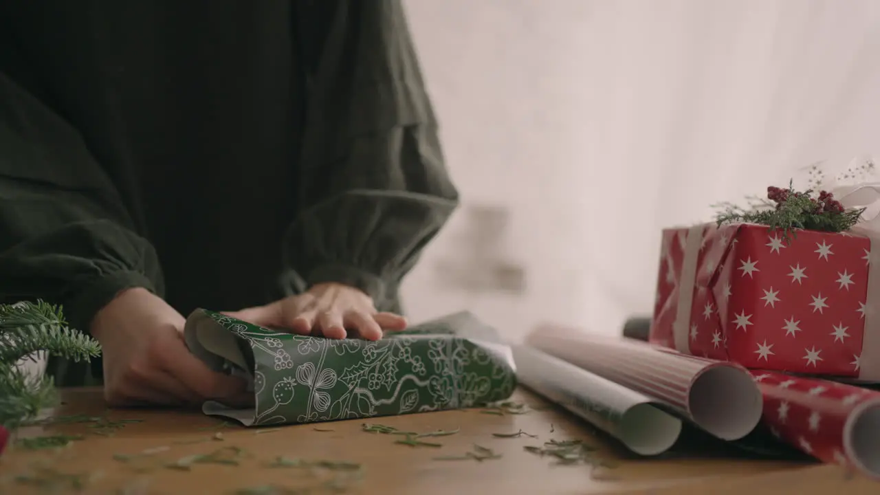 A close-up of the hand of a woman wraps her hands around a box in a wrapping paper with a Christmas ornament professional decorator gift wrapper