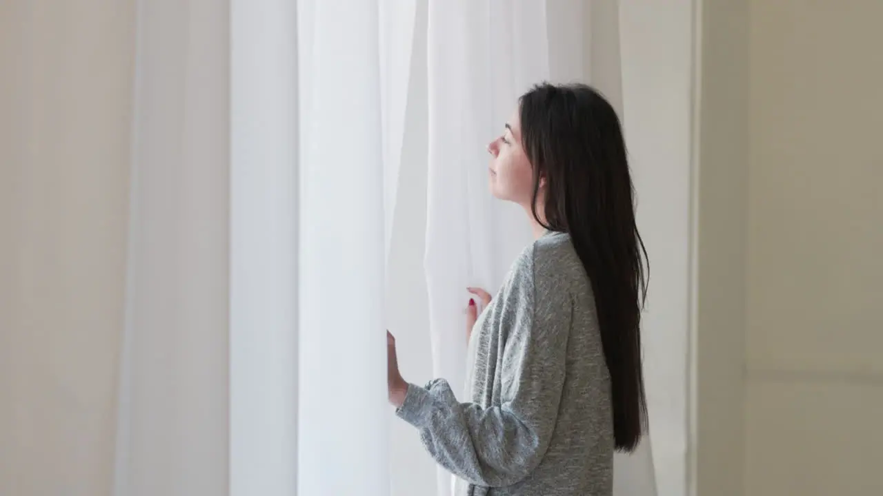 Pensive Woman Standing Looking Outside Through A Window At Home In The Morning