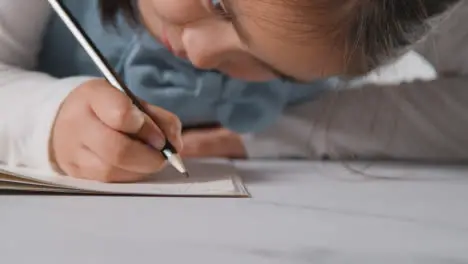 Studio Shot Of Young Girl At Table Concentrating On Writing In School Book