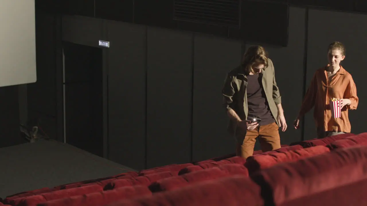 Couple Entering A Movie Theater And Finding Seats Using Phone Flashlight Before The Film Starts