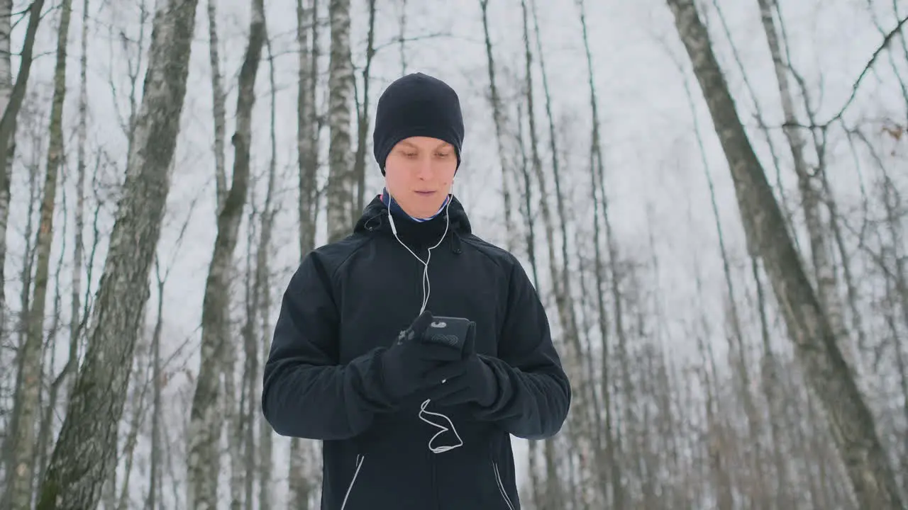 A young man in a black trigger in the winter is preparing to jog in the park includes running music on a smartphone and runs with a voice assistant through the forest doing business and leading a healthy lifestyle