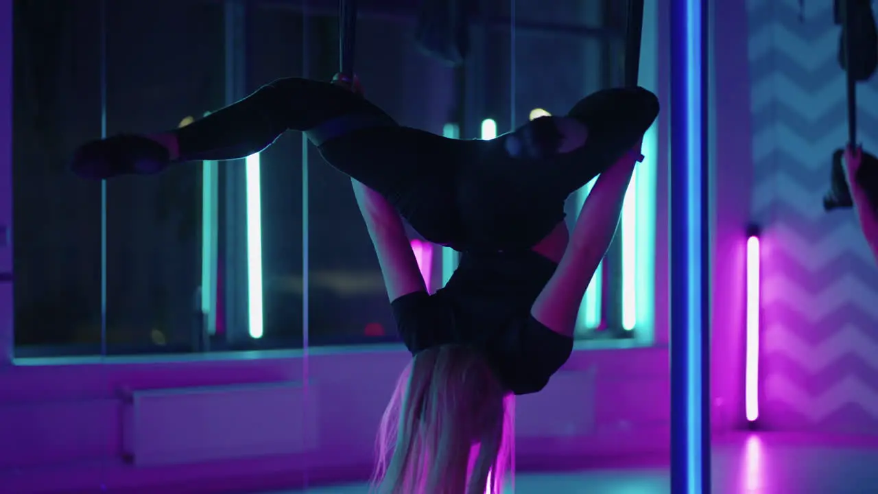 A woman does yoga and stretching on a hanging hammock in neon light A woman is flying in a hammock in the studio doing stretching and body exercises Exercises in the air