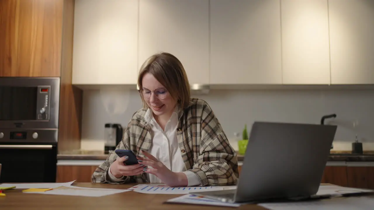 Millennial woman employee sit by work desk chat in phone messenger app taking break in computer job Young lady worker manager browse web in mobile application on smartphone office from home