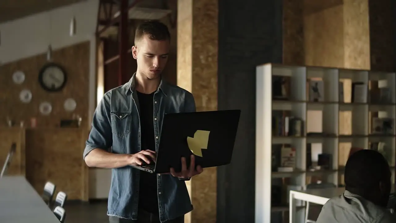 Attractive Concentrated Young Business Man Is Walking With Black Laptop In His Hand And Typing