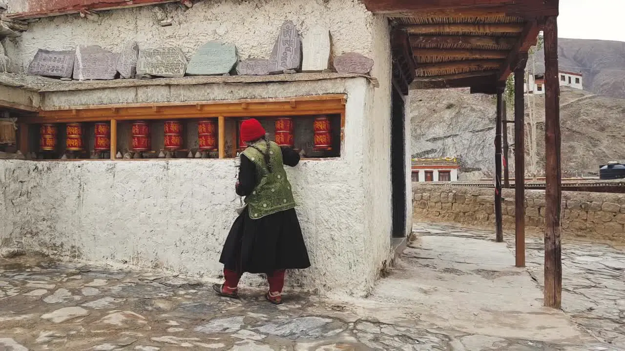 An Old Woman walking and turning the Prayer wheels in Lamayuru Monastery