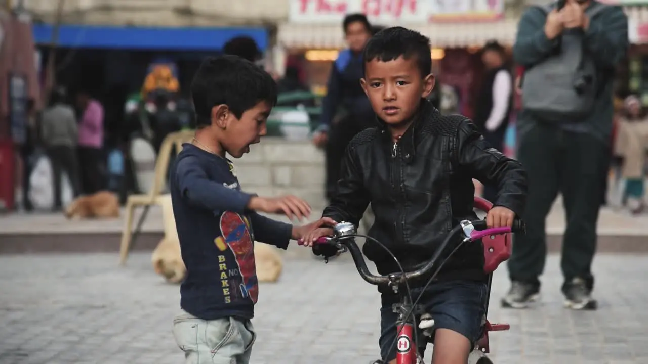 Two kids cycling and playing in the street market of the Leh