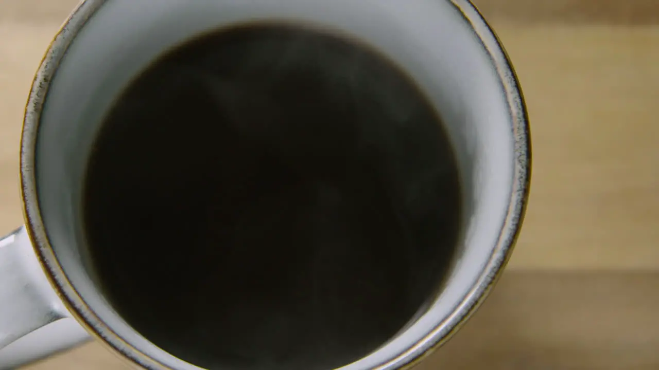 PAN LEFT a steaming cup of black coffee on a wooden table 60fps