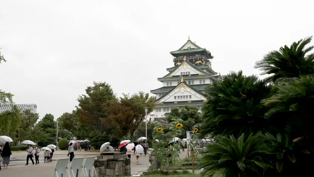 Visitors With Umbrellas Walking Towards Osaka Castle On Rainy Overcast Day