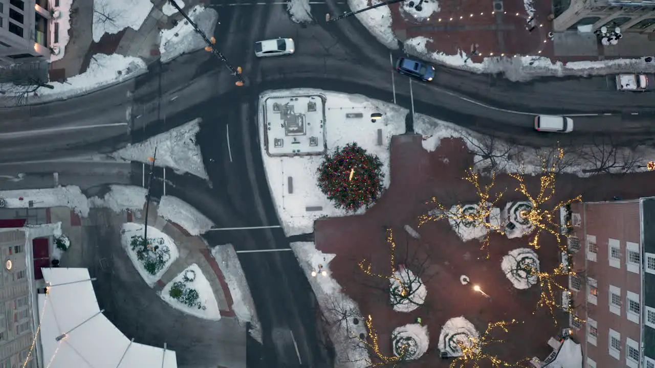 Top down aerial of traffic passing through urban city street with snow and Christmas tree lights