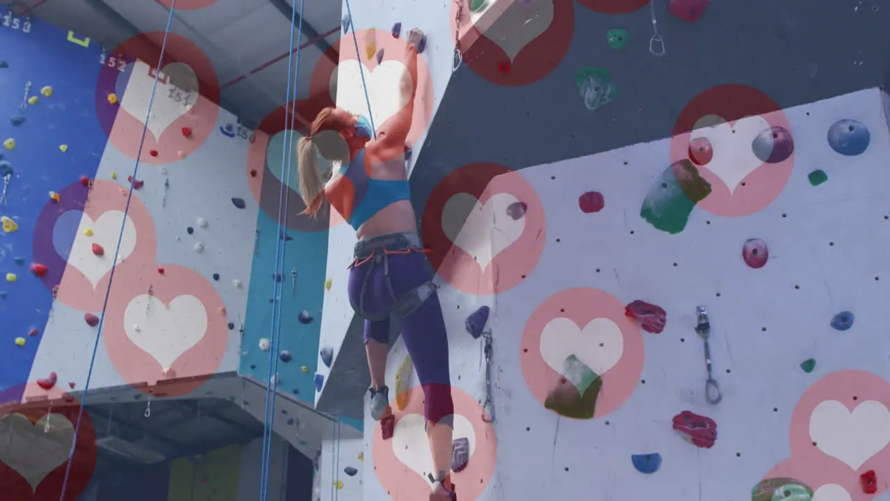 Multiple heart icons floating against caucasian fit woman wall climbing at the gym