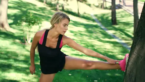 Sport woman stretching legs on tree trunk before workout outdoor in summer park