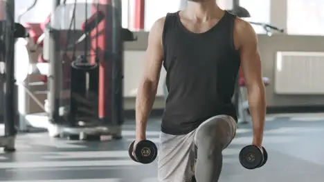 Handsome man doing lunges exercise with dumbbells in fitness club