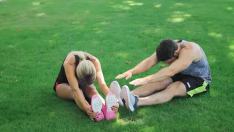 Young couple stretching before fitness workout at green grass in summer park