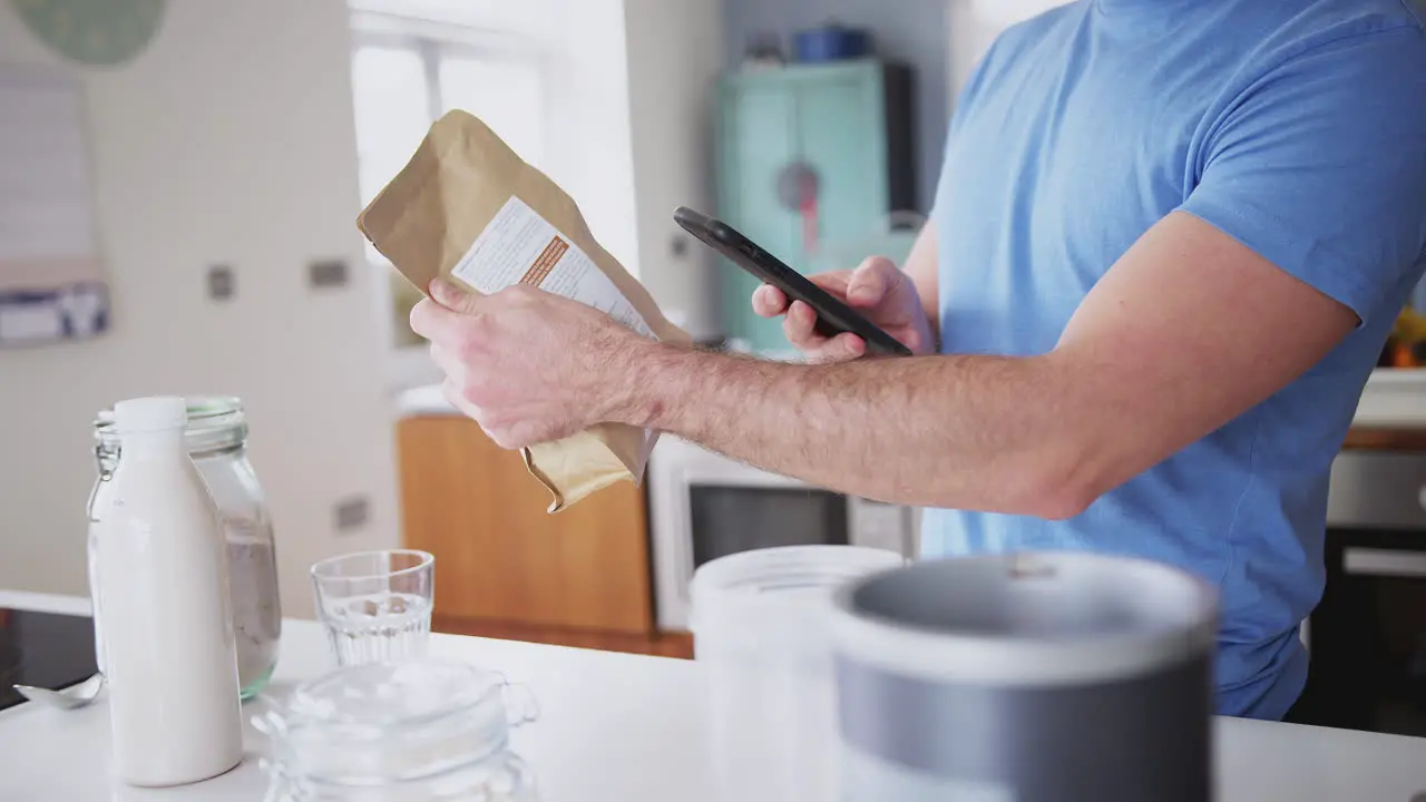 Man Wearing Fitness Clothing Scanning QR Code On Food Packaging To Find Nutritional Information